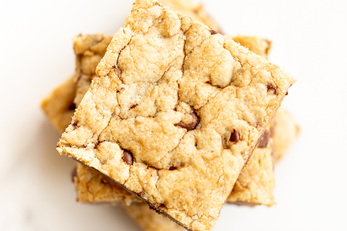 Salted caramel chocolate chip cookie bars cut into squares on a white surface. 