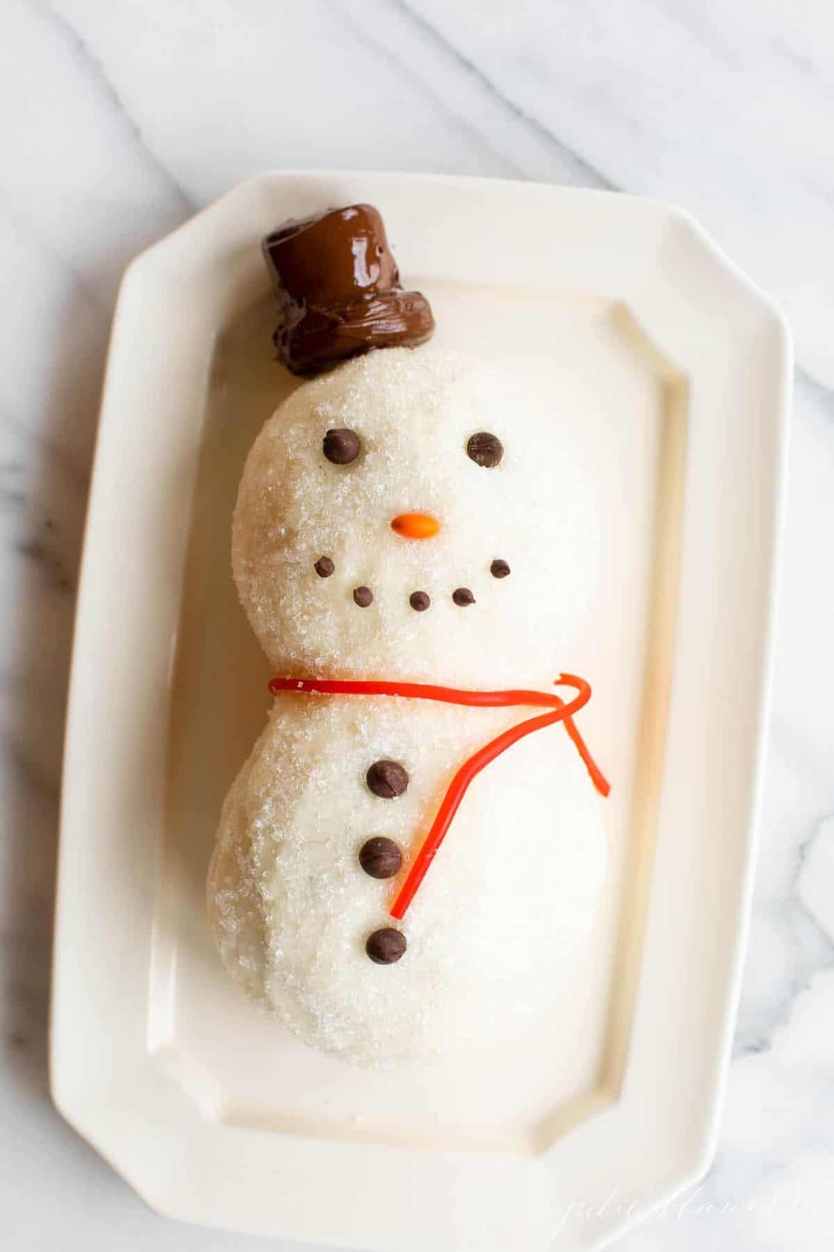 A sugared snowman cheese ball recipe, licorice for scarf on a white platter.