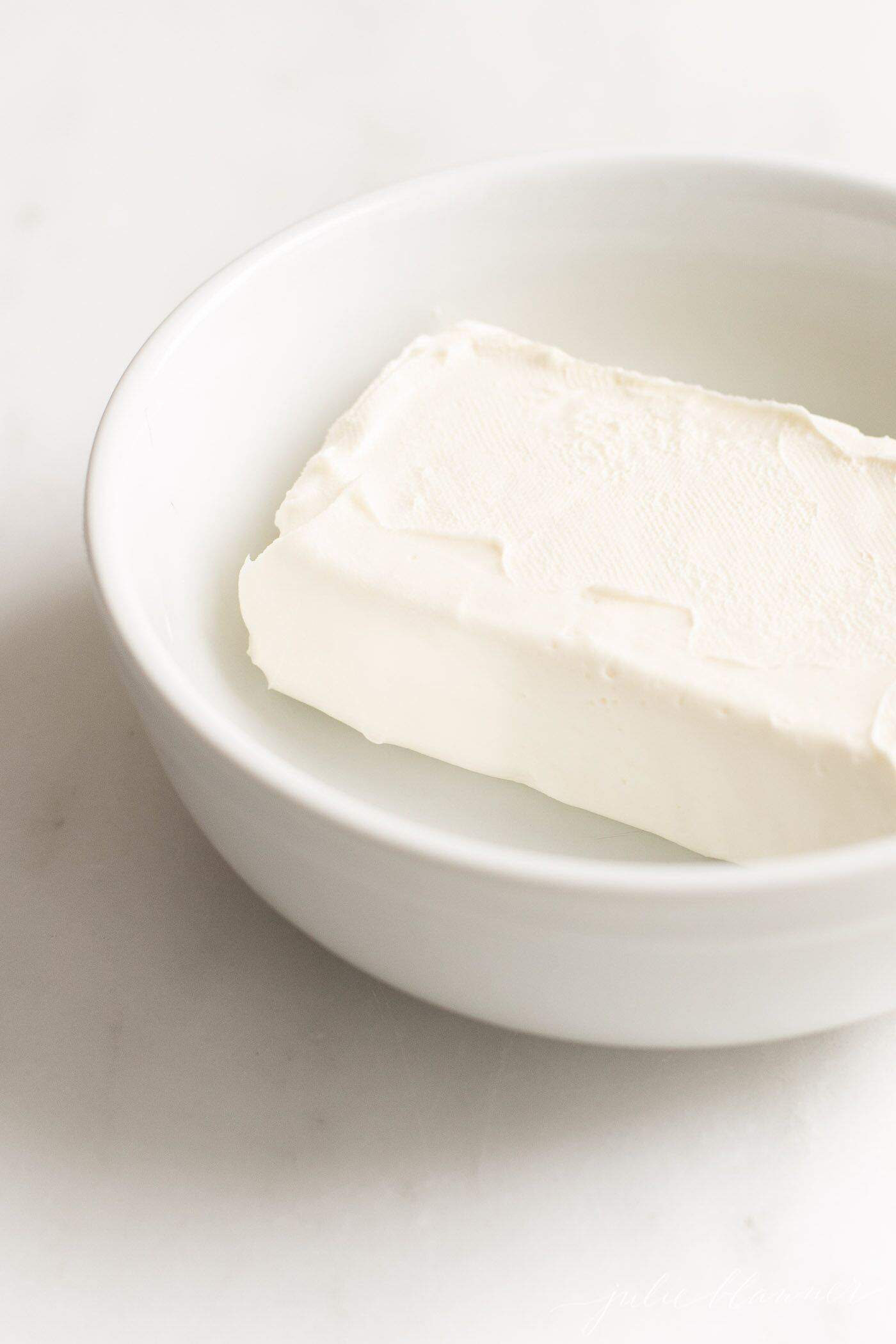 White bowl with a block of cream cheese inside.