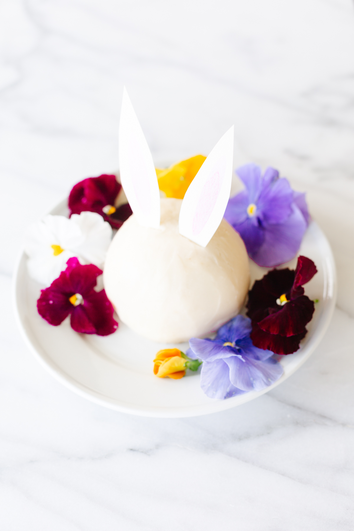 A bunny shaped cheese ball recipe adorned with flowers displayed on a white plate.