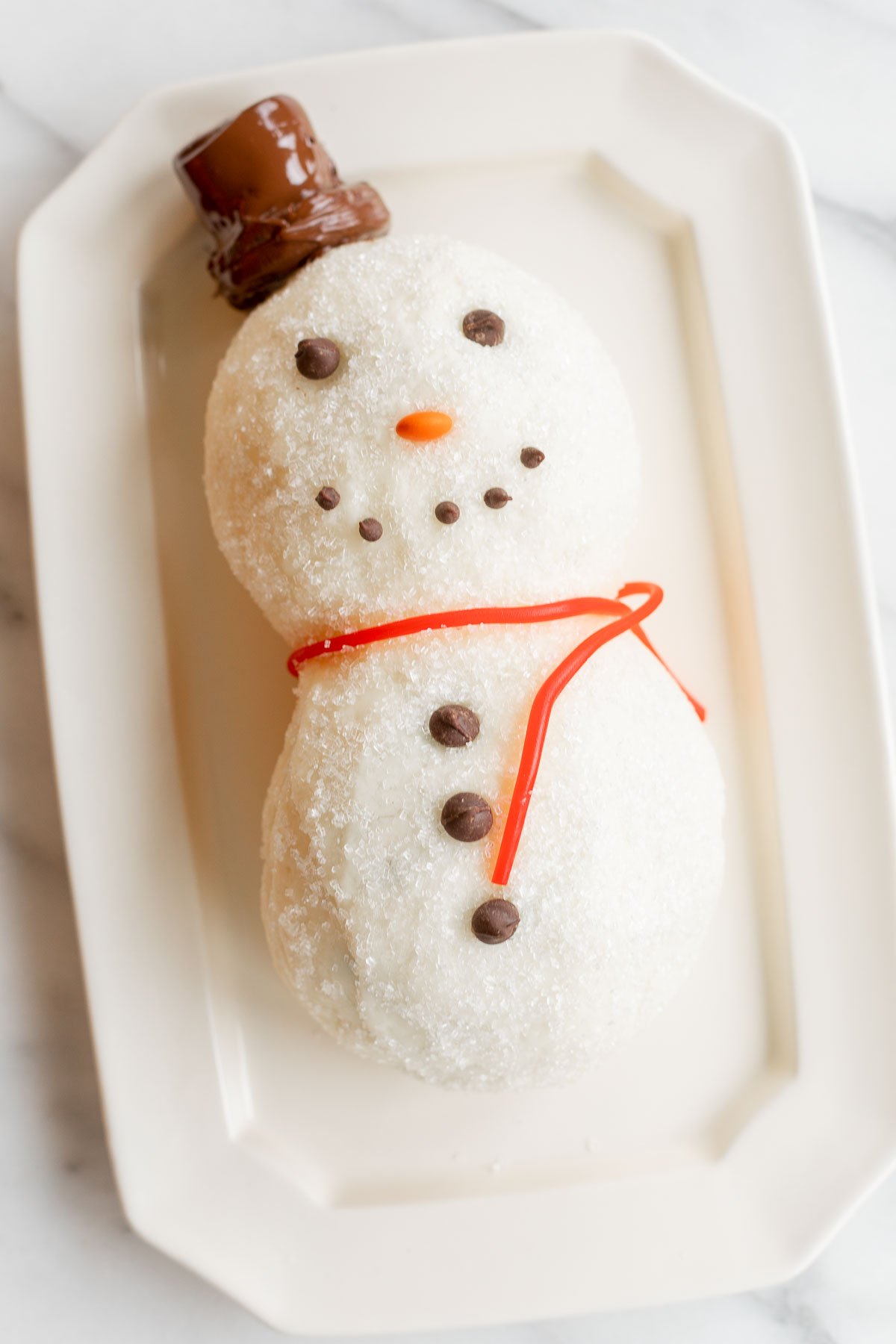 A cheesy snowman shaped doughnut on a plate.