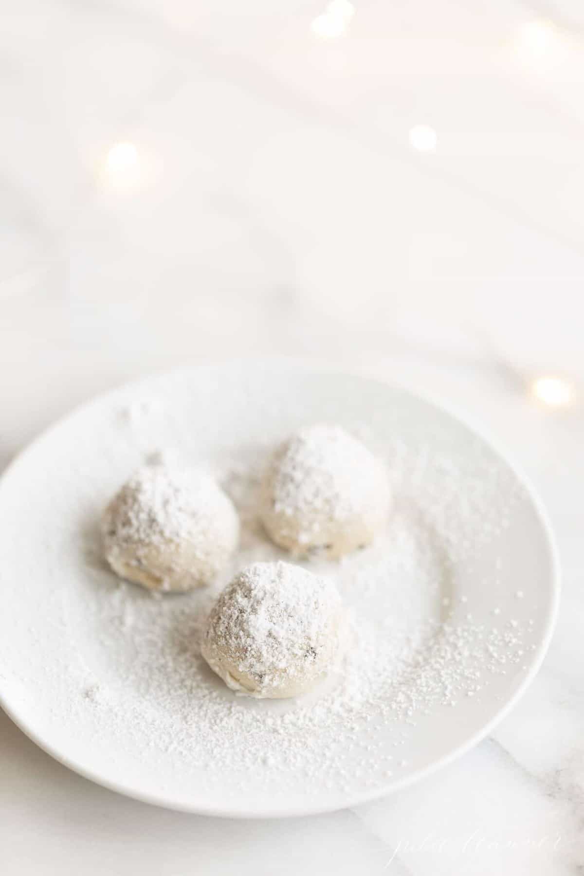 A small white plate with a group of three pecan snowball cookies.