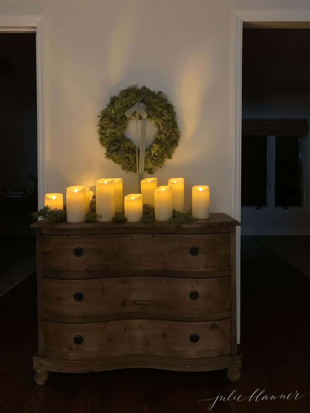 Entryway at night, candles and evergreen on a console table, wreath above.