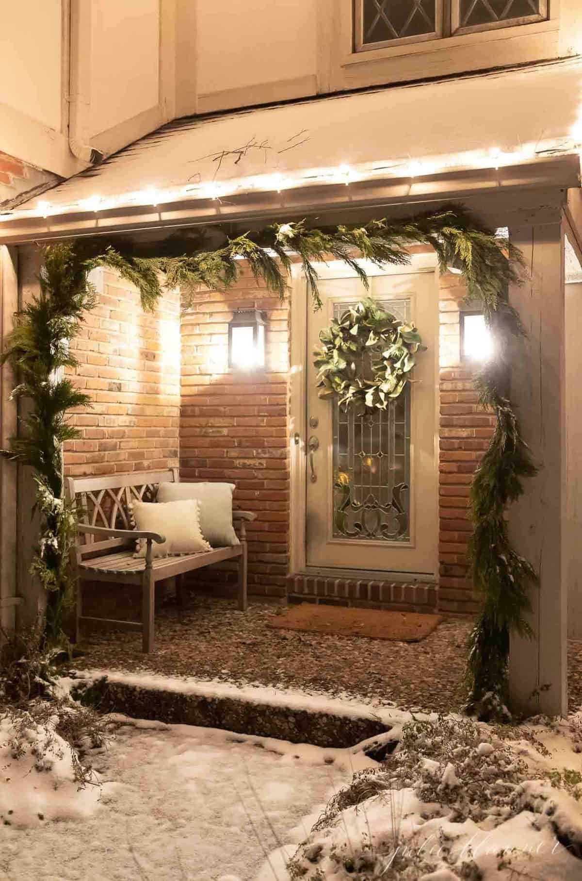 Exterior of a home, snow on the ground and greenery garland on posts for Christmas.