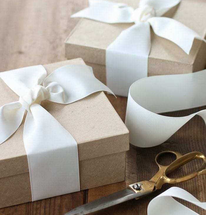 A wooden surface with Kraft boxes wrapped in white ribbon.