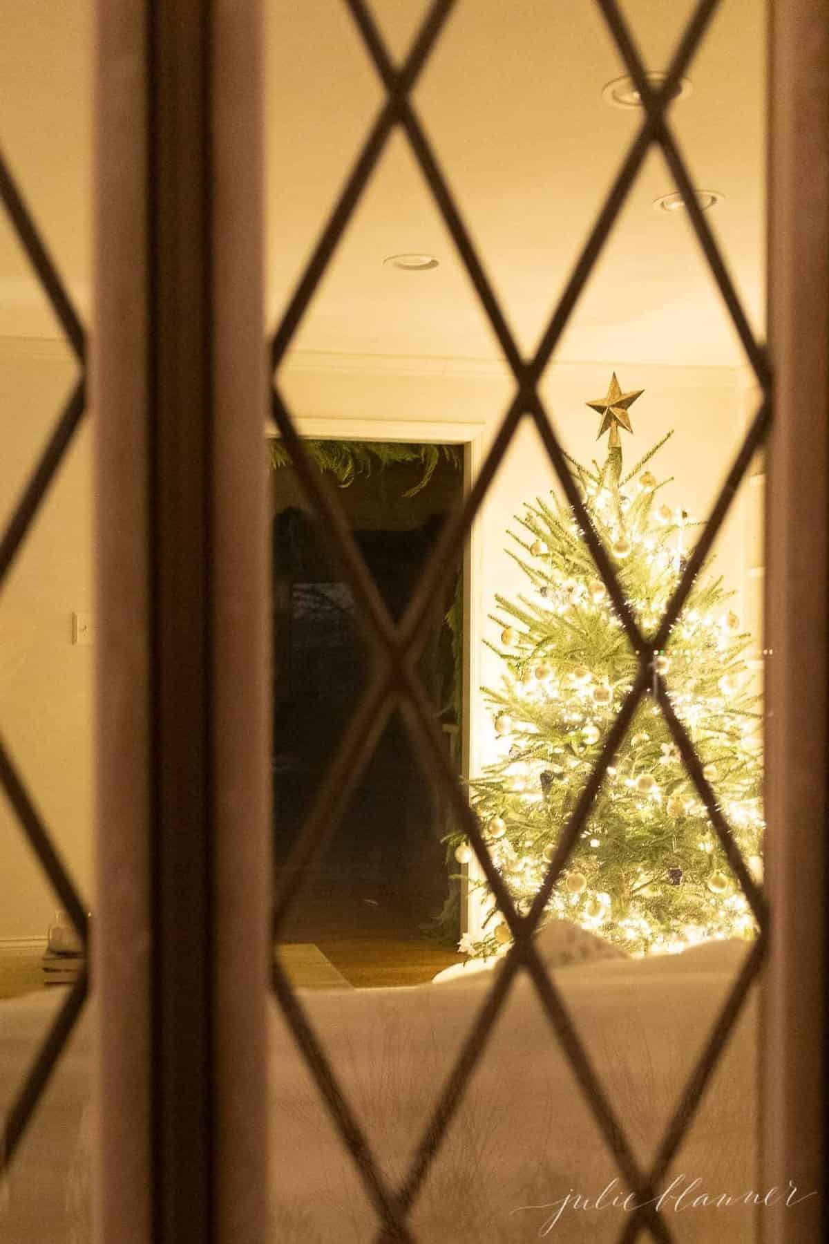 Looking from outside into a living room Christmas tree scene, at night.