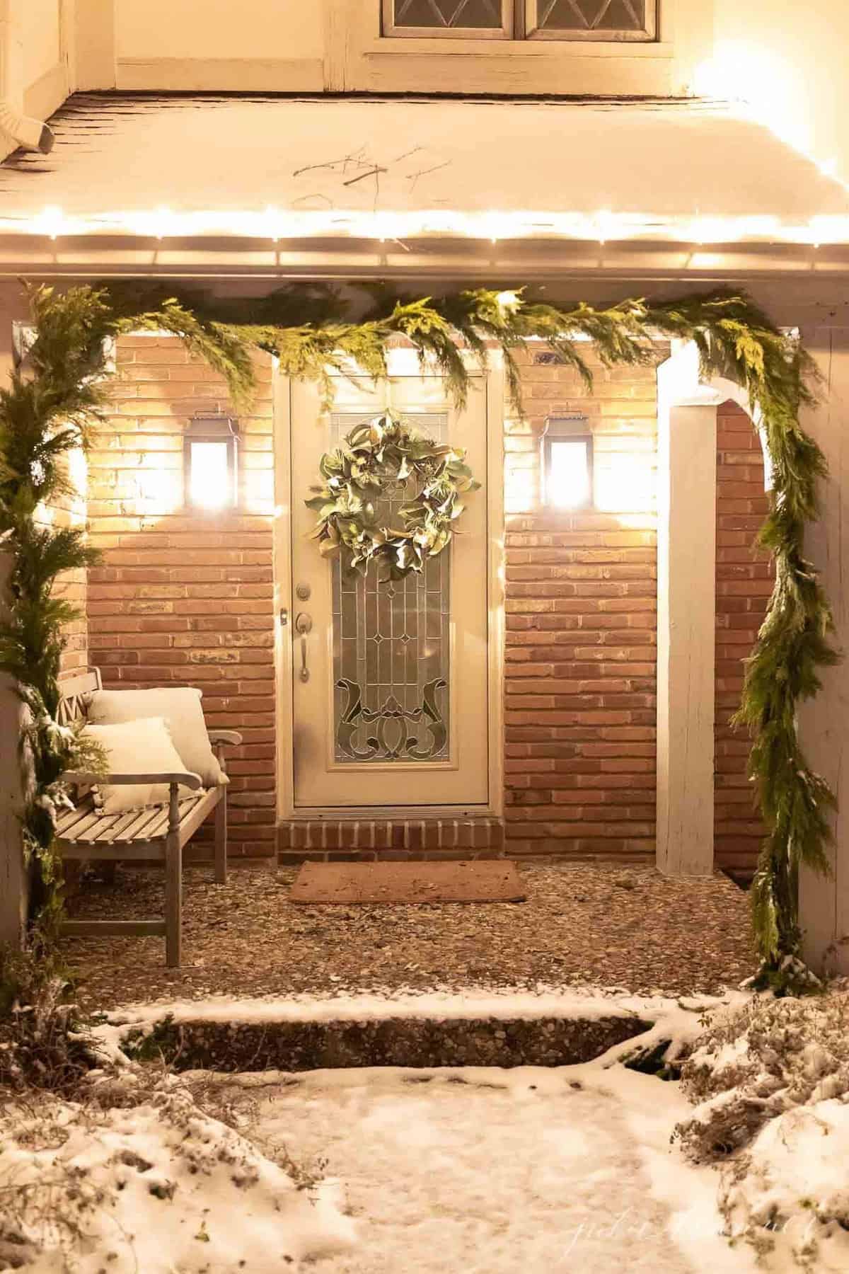 Exterior of a home, snow on the ground and greenery garland on posts for Christmas.