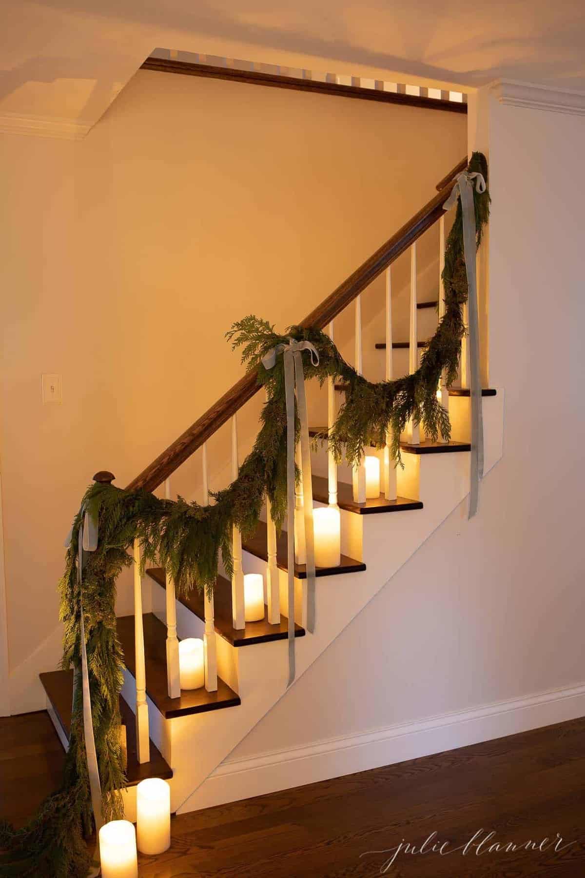 White walls, wooden staircase decorated with candles and garland at Christmas.