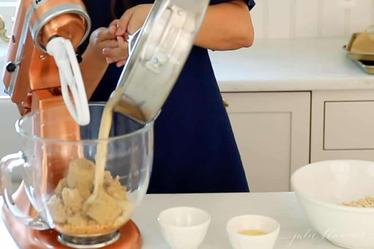 A woman in a navy dress standing behind a copper stand mixer making oatmeal lace cookies.