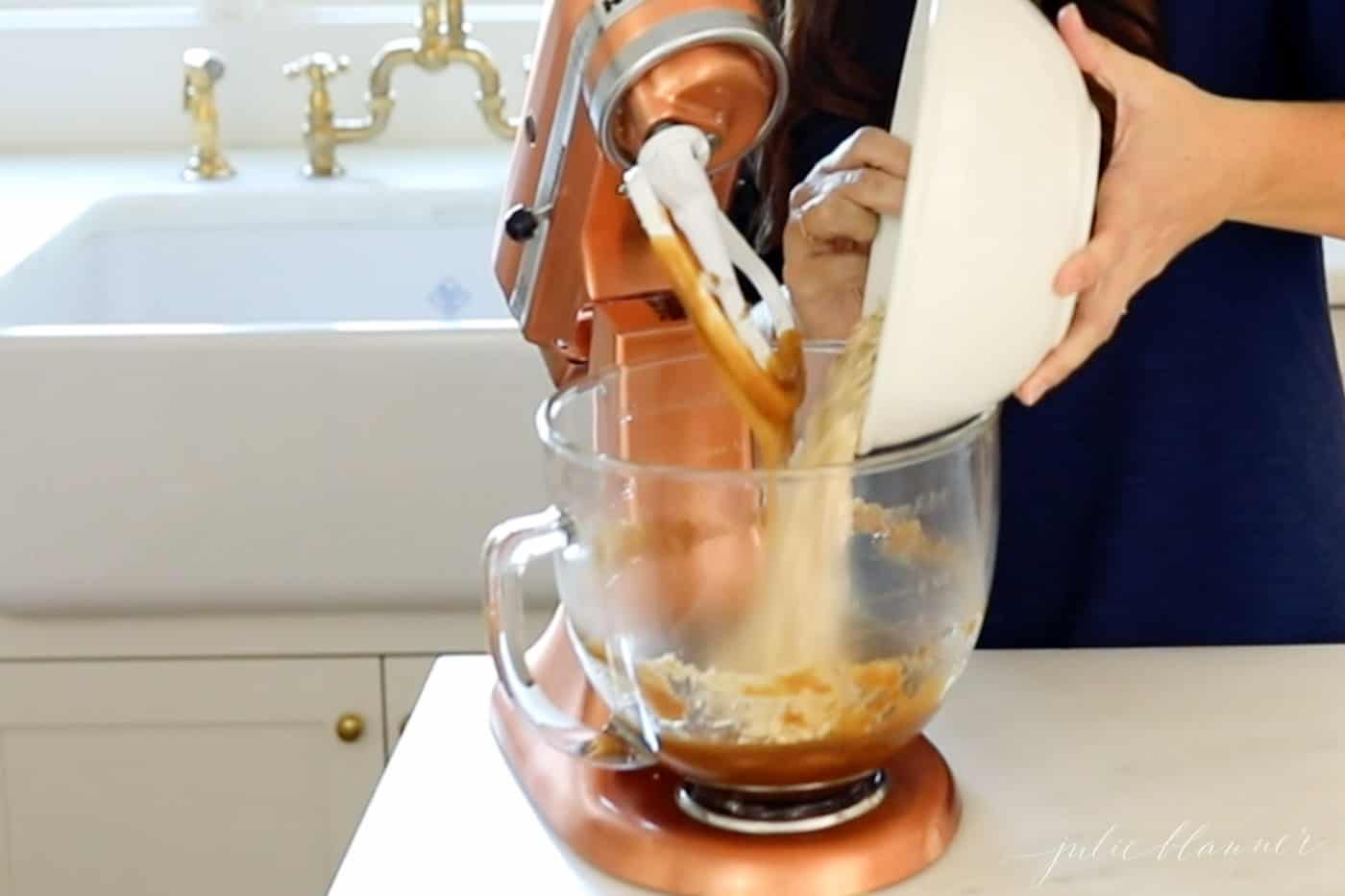A woman in a navy dress standing behind a copper stand mixer making oatmeal lace cookies.