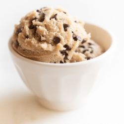 A small white bowl full of edible cookie dough with chocolate chips, on a marble surface