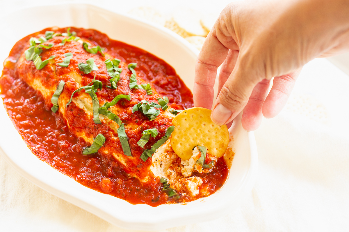 A person is dipping a chip into a dish of queso de cabra con tomate enchiladas.