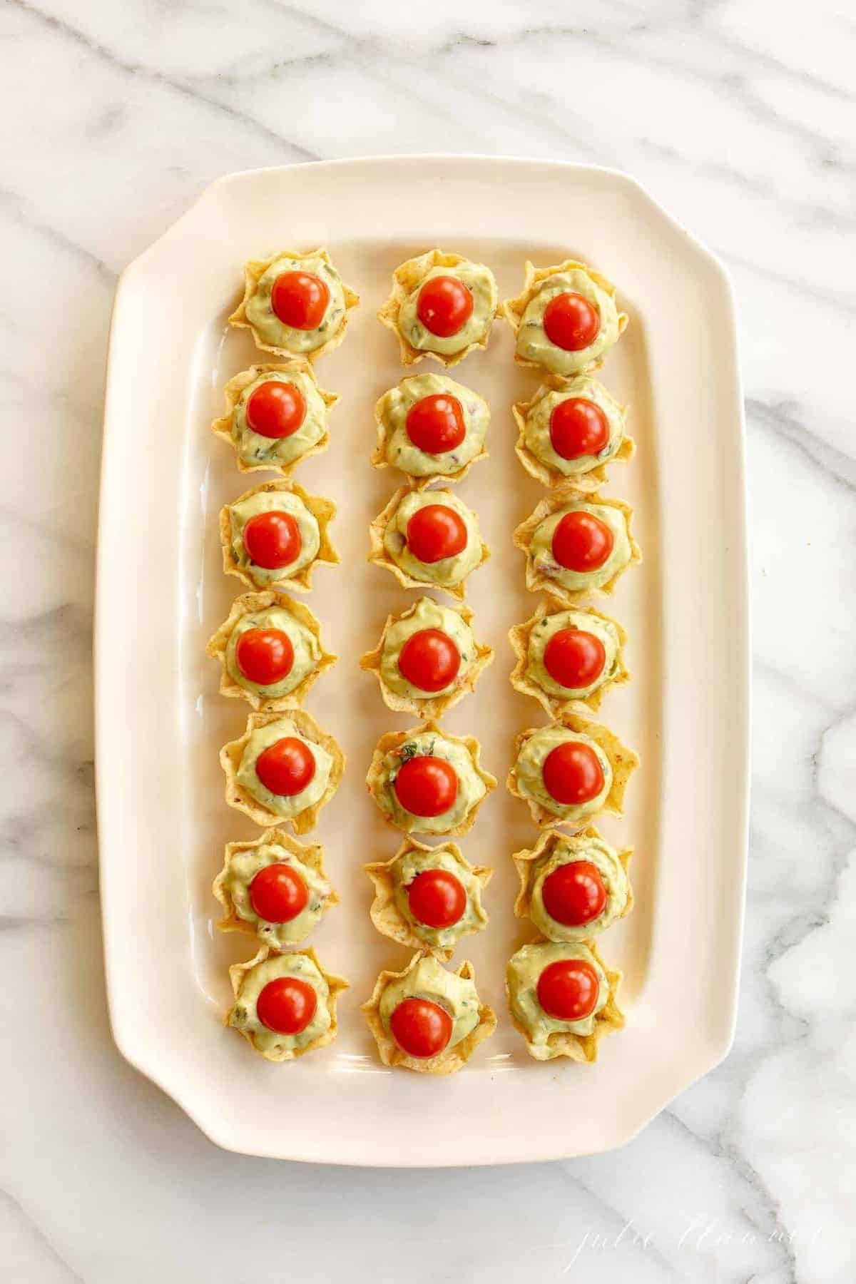 Marble surface, white platter filled with guacamole bites appetizer.