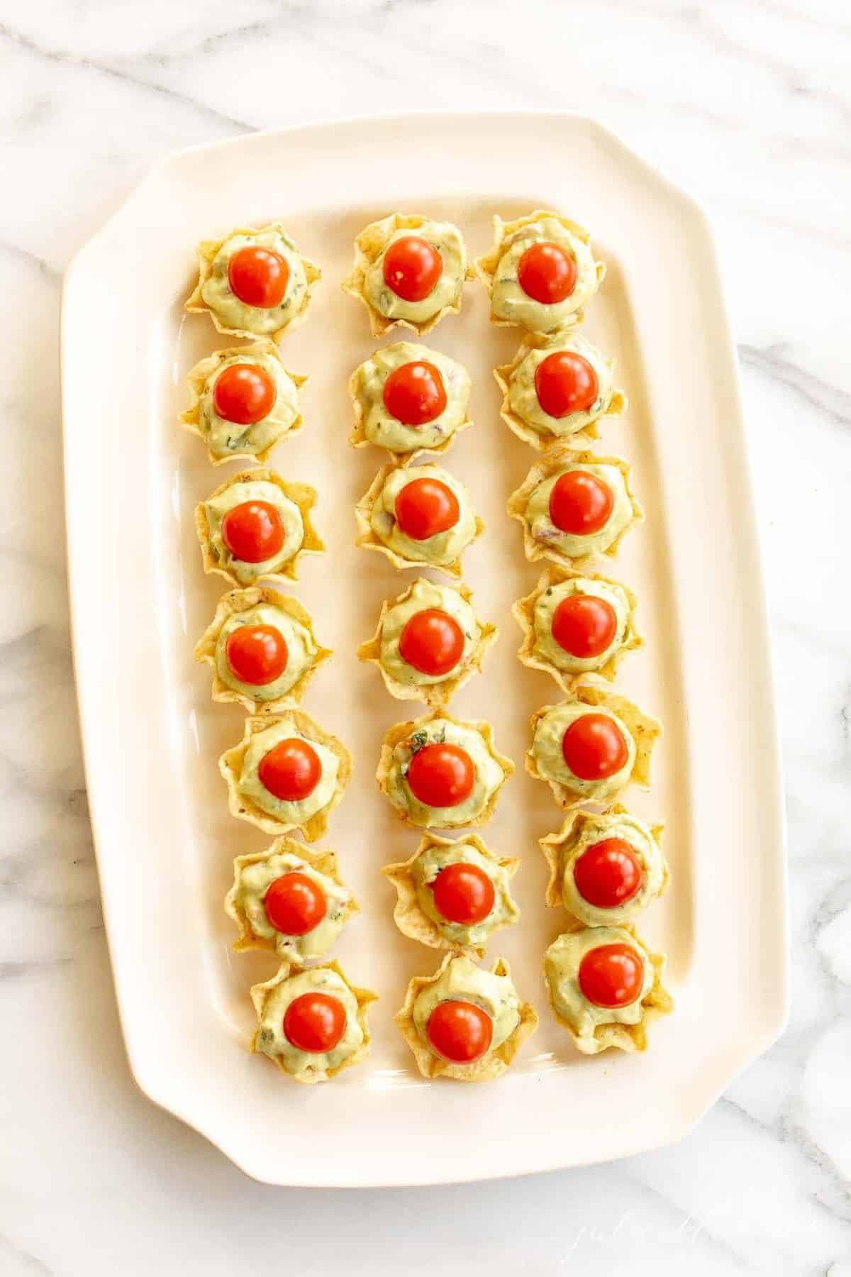 Guacamole bites on a white platter with a marble background.