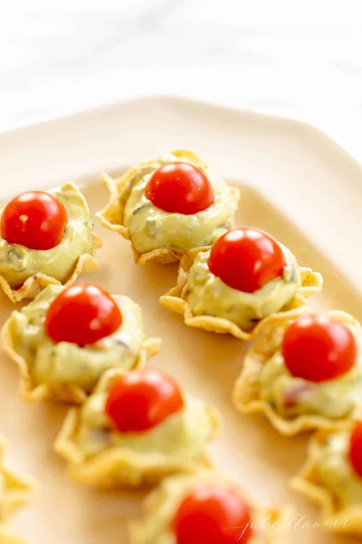 A close up of guacamole bites on a white platter with a marble background.