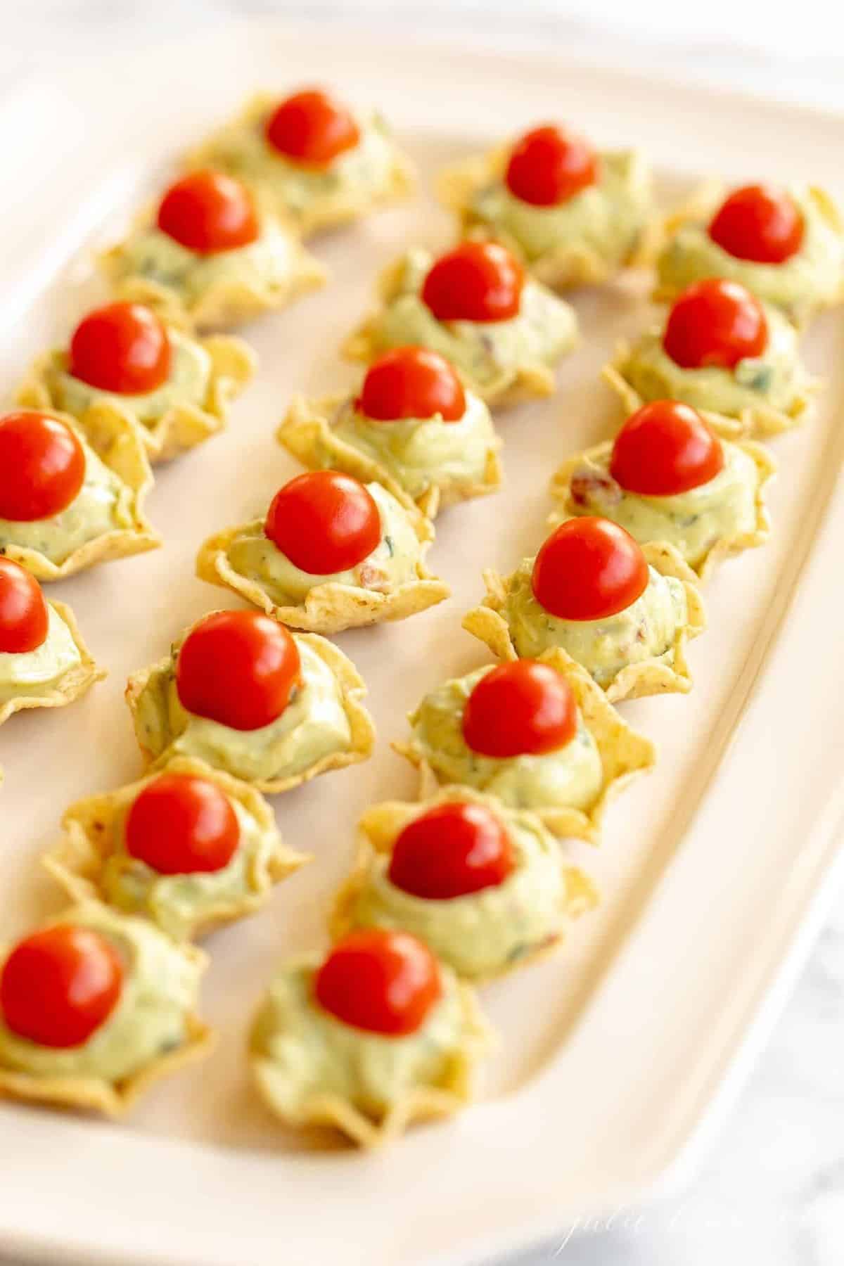 A platter filled with chips, served as guacamole bites, topped with a slice of cherry tomato.