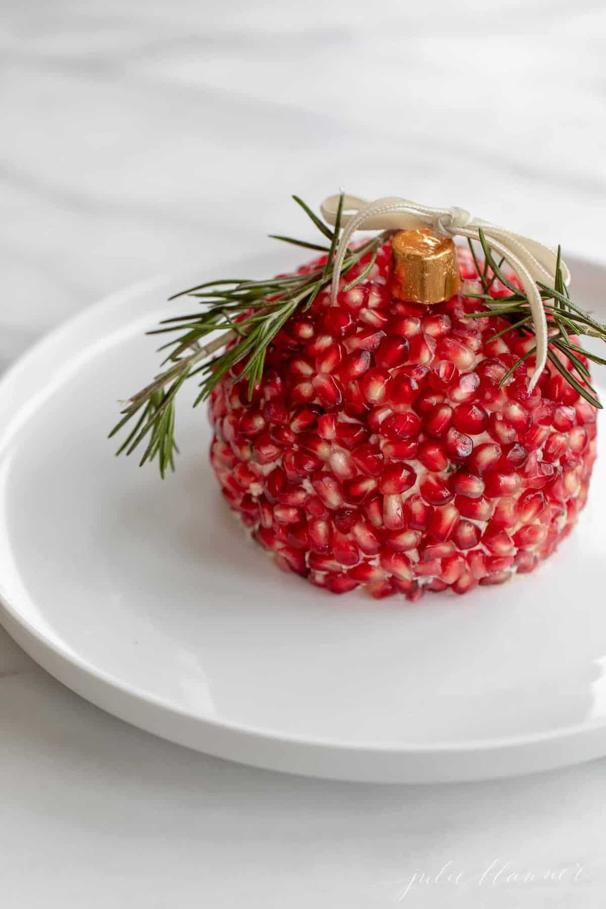 A holiday cheese ball in the shape of a Christmas ornament, covered in pomegranate seeds.
