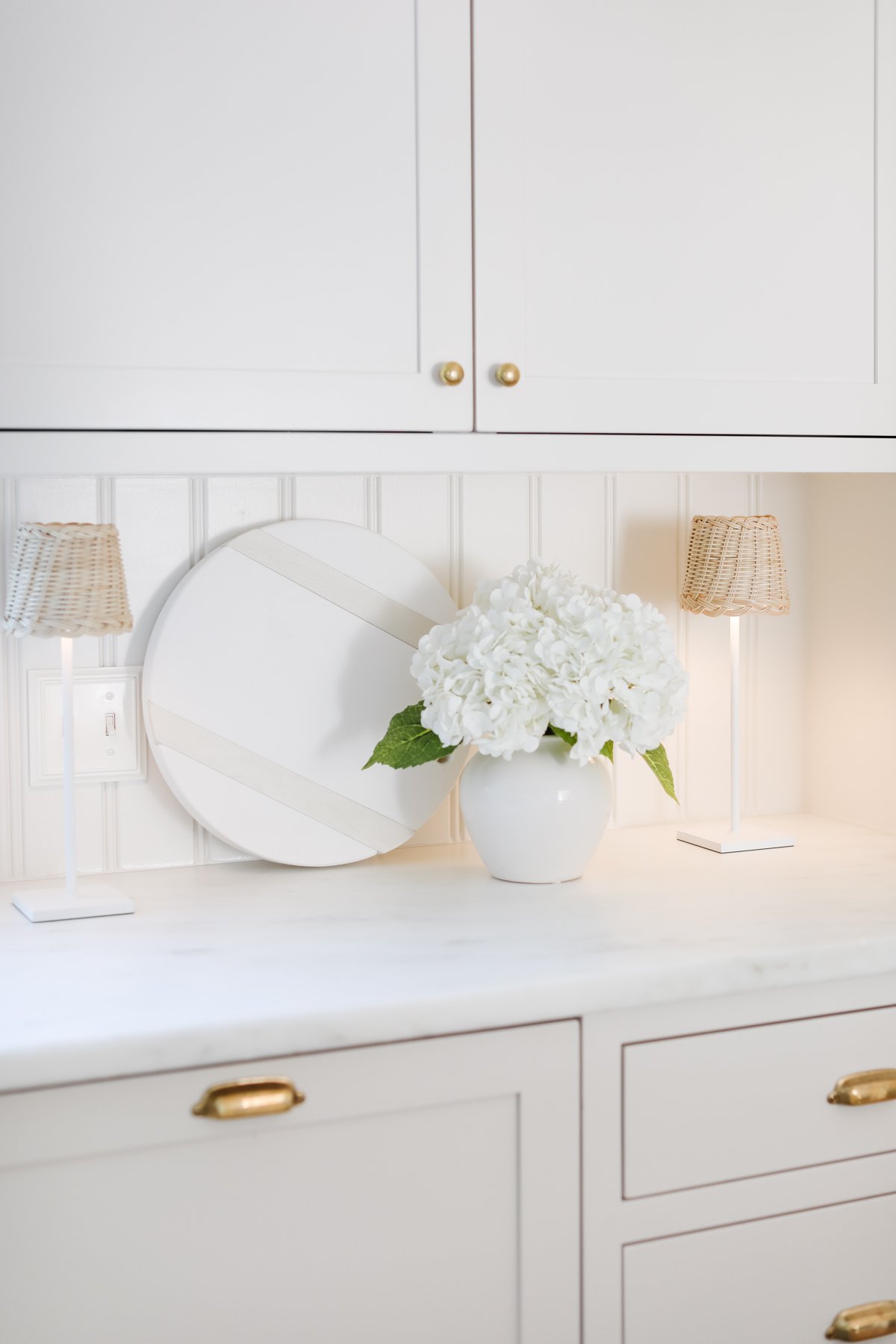 A kitchen with led lamps, a vase of hydrangea and a white charcuterie board on the countertop.