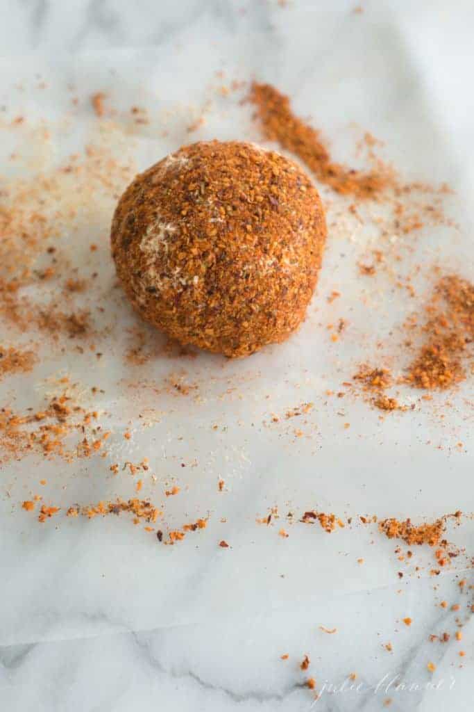 A simple cheeseball covered in spices on a marble surface.