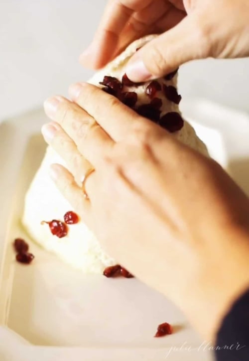 Hands pressing dried cranberries onto a cheese ball
