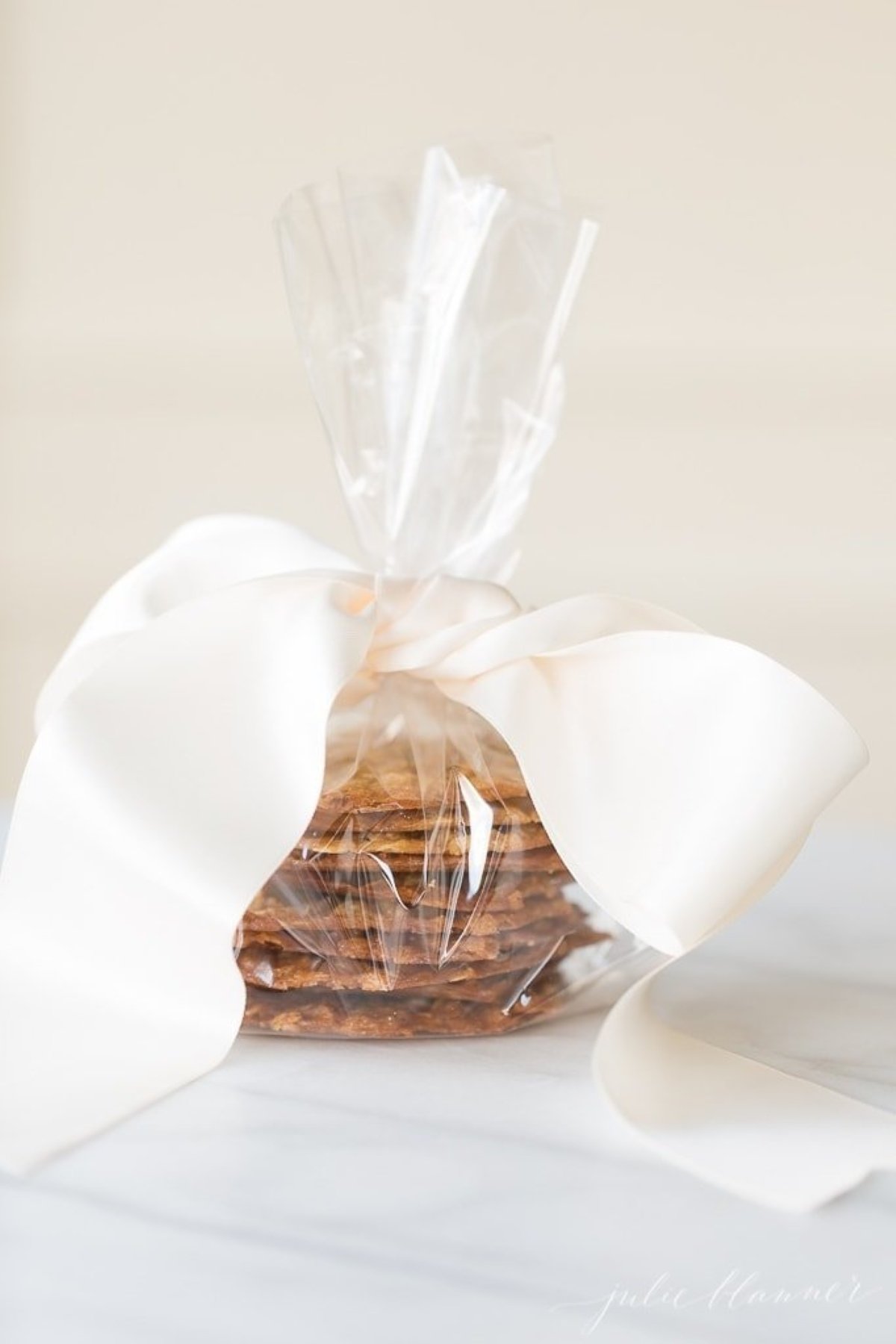 A stack of lace cookies in a cellophane bag, tied with a wide ivory bow.