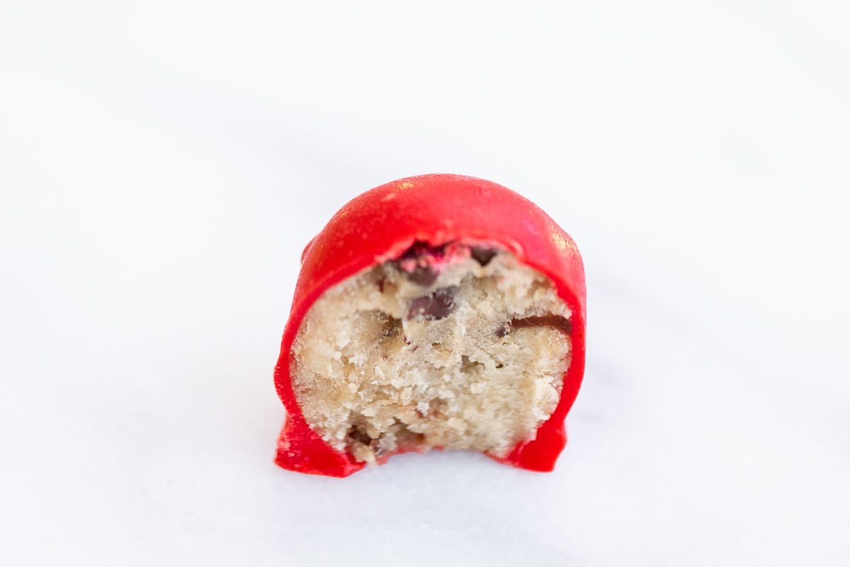A single red Rudolph nose on a marble surface, bitten half through to see the edible cookie dough inside.