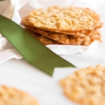 A stack of oatmeal lace cookies on a white surface, with a touch of green ribbon in the corner