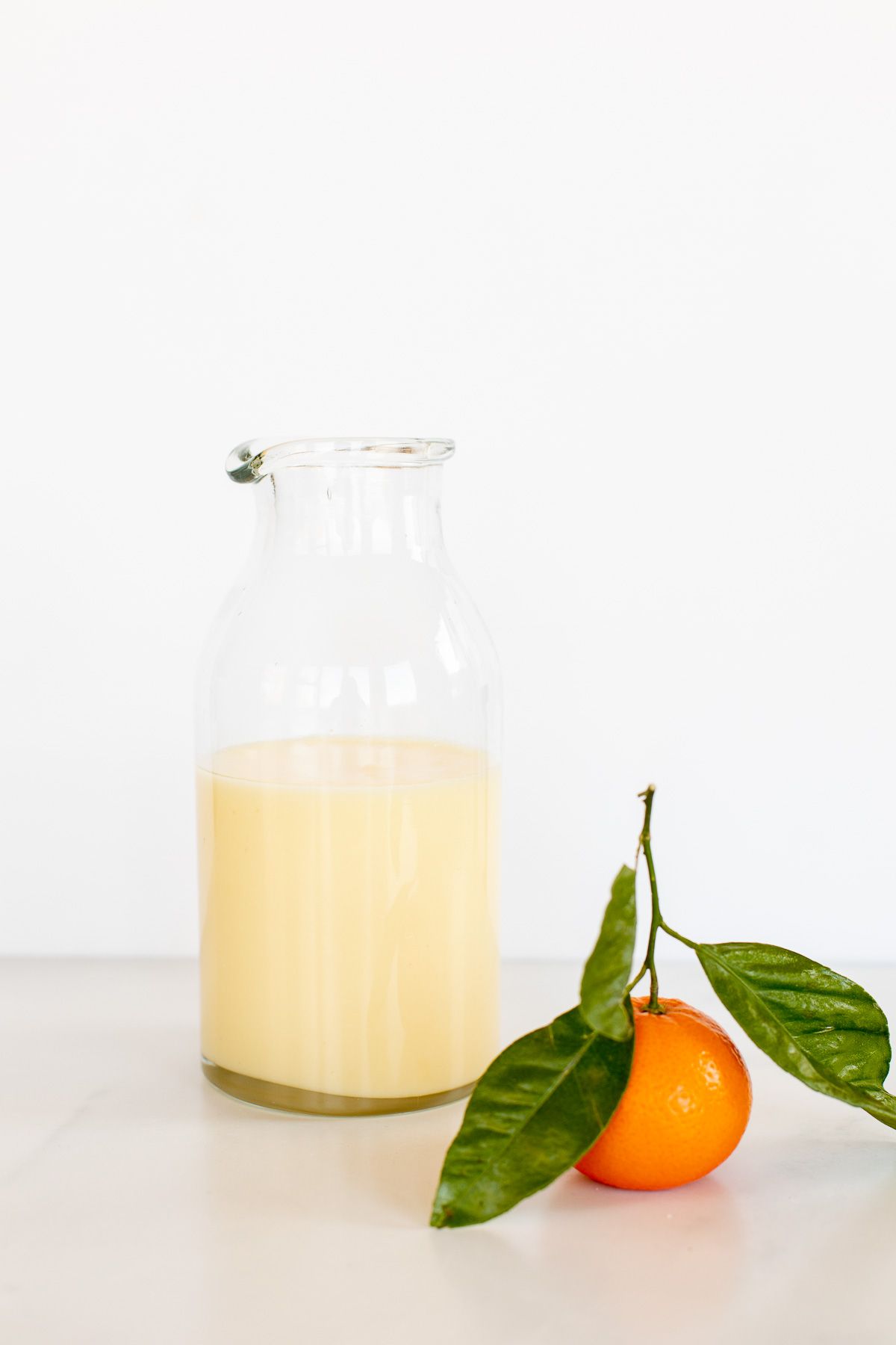 A glass jar of orange glaze, with a small orange in front. 