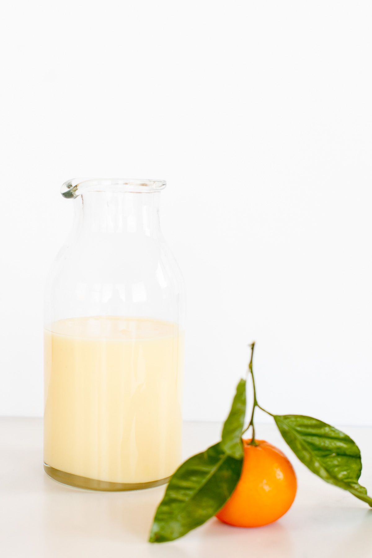 A glass jar of orange glaze, with a small orange in front.