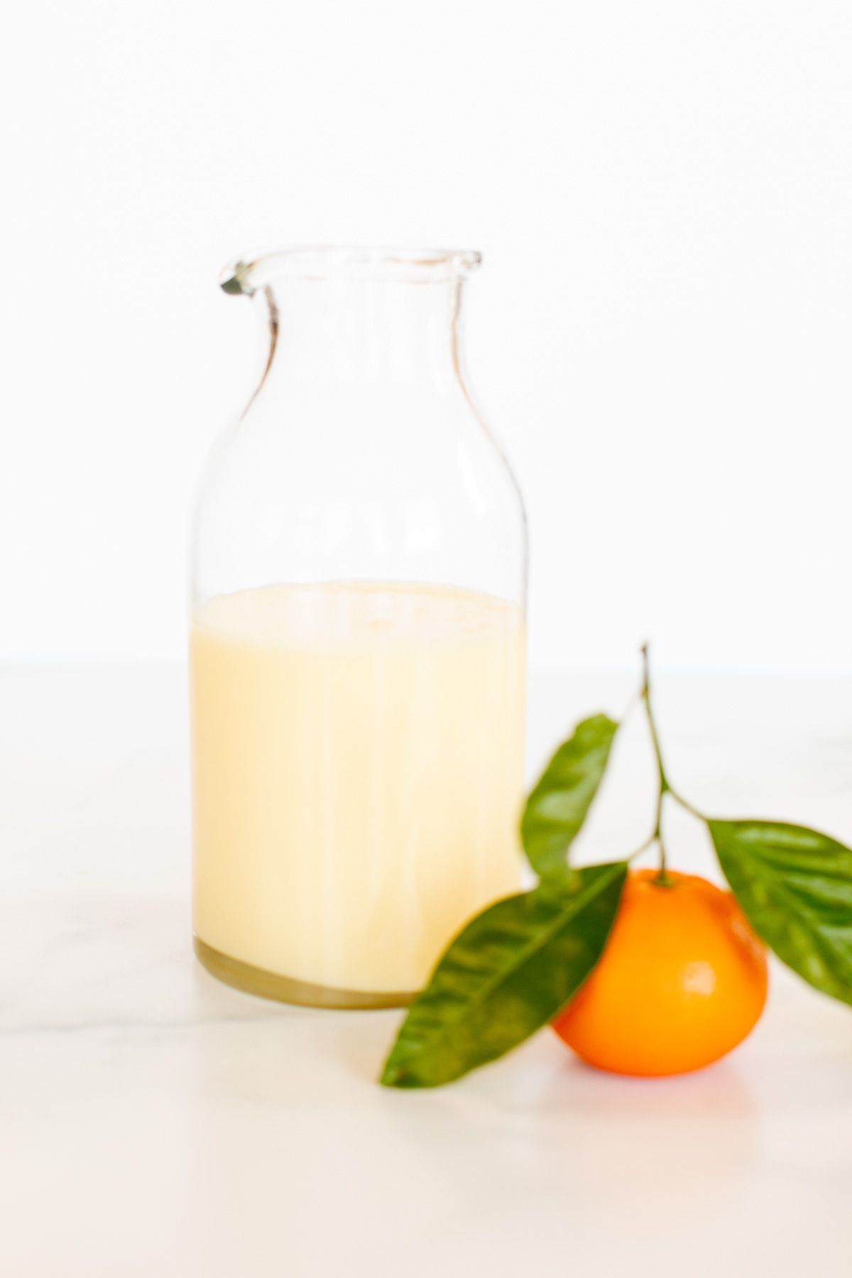 A glass jar of orange glaze, with a small orange in front.