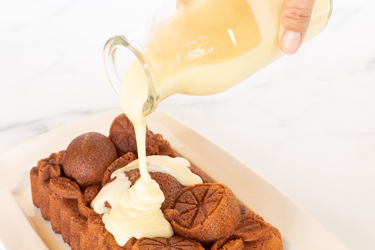 A glass jar of orange glaze pouring over an orange pound cake