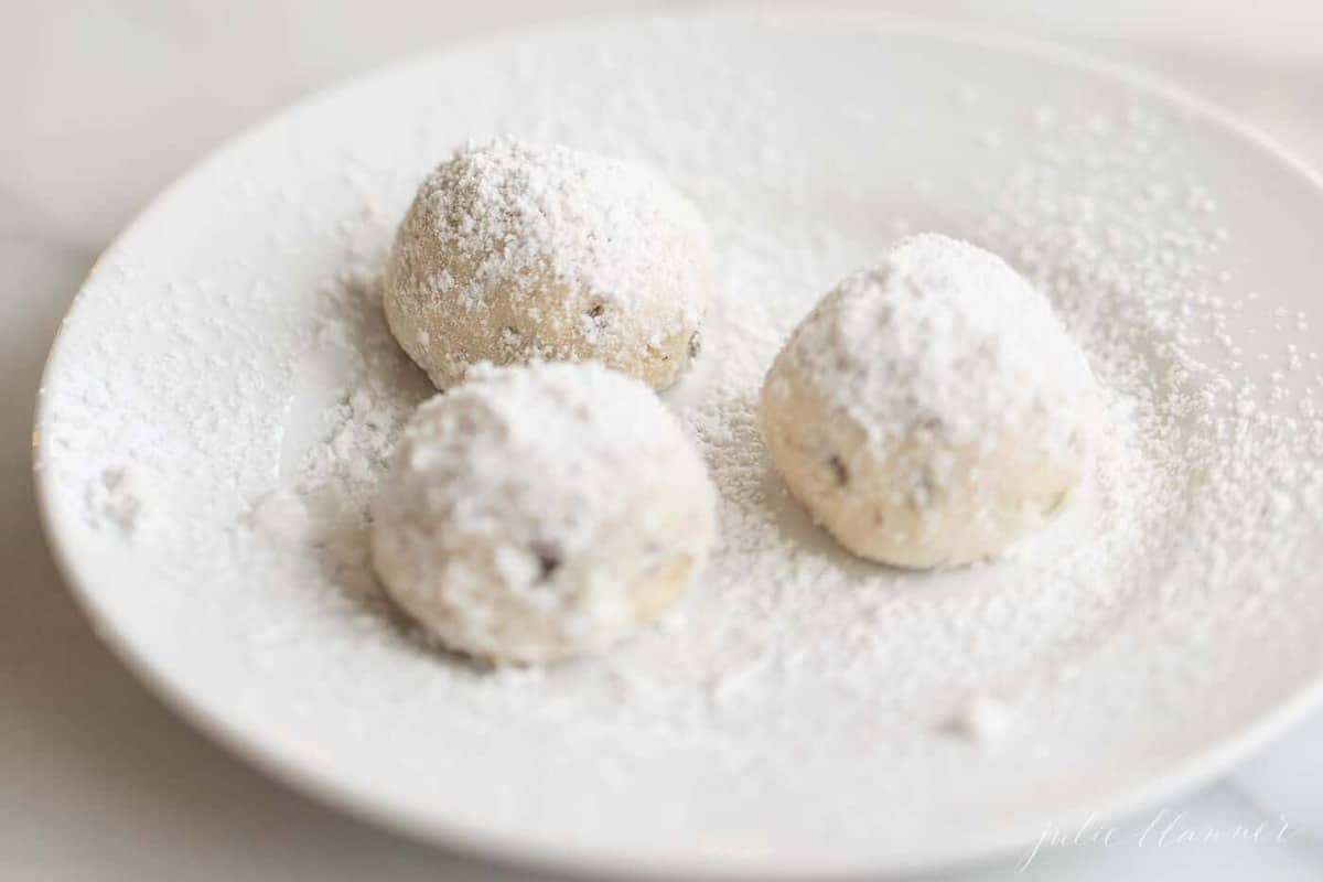 A small white plate with a group of three pecan snowball cookies.