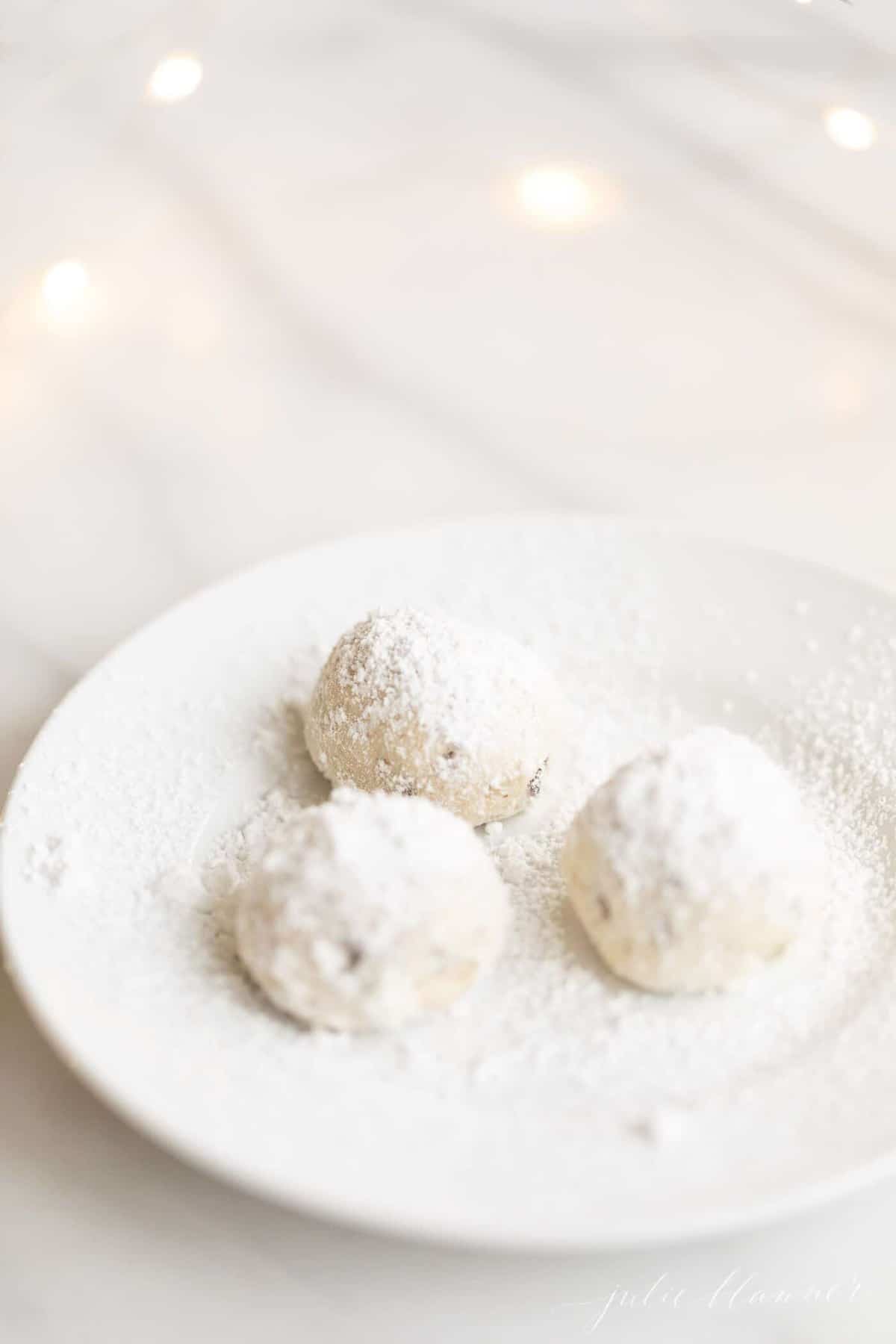 A small white plate with a group of three pecan snowball cookies.