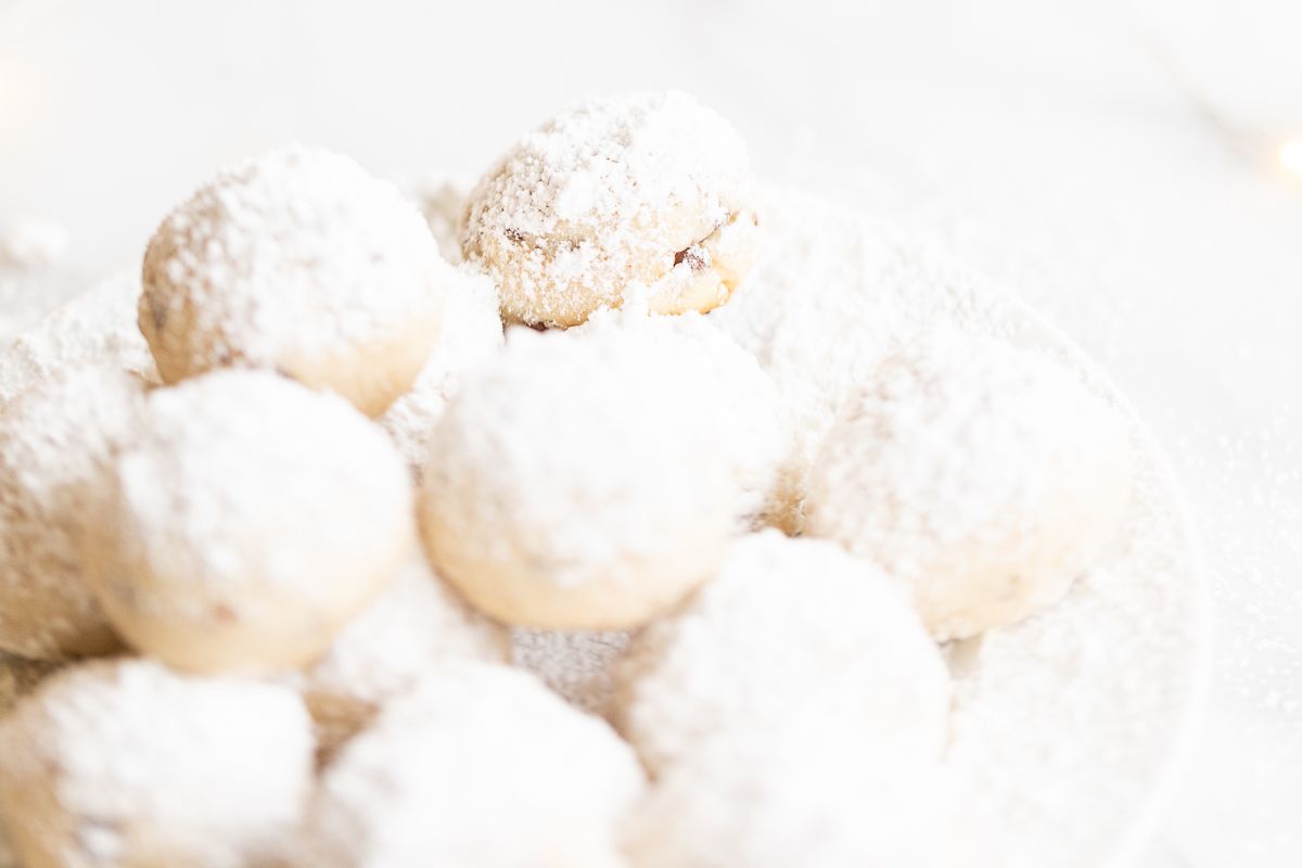 A white plate of pecan snowball cookies covered in powdered sugar.
