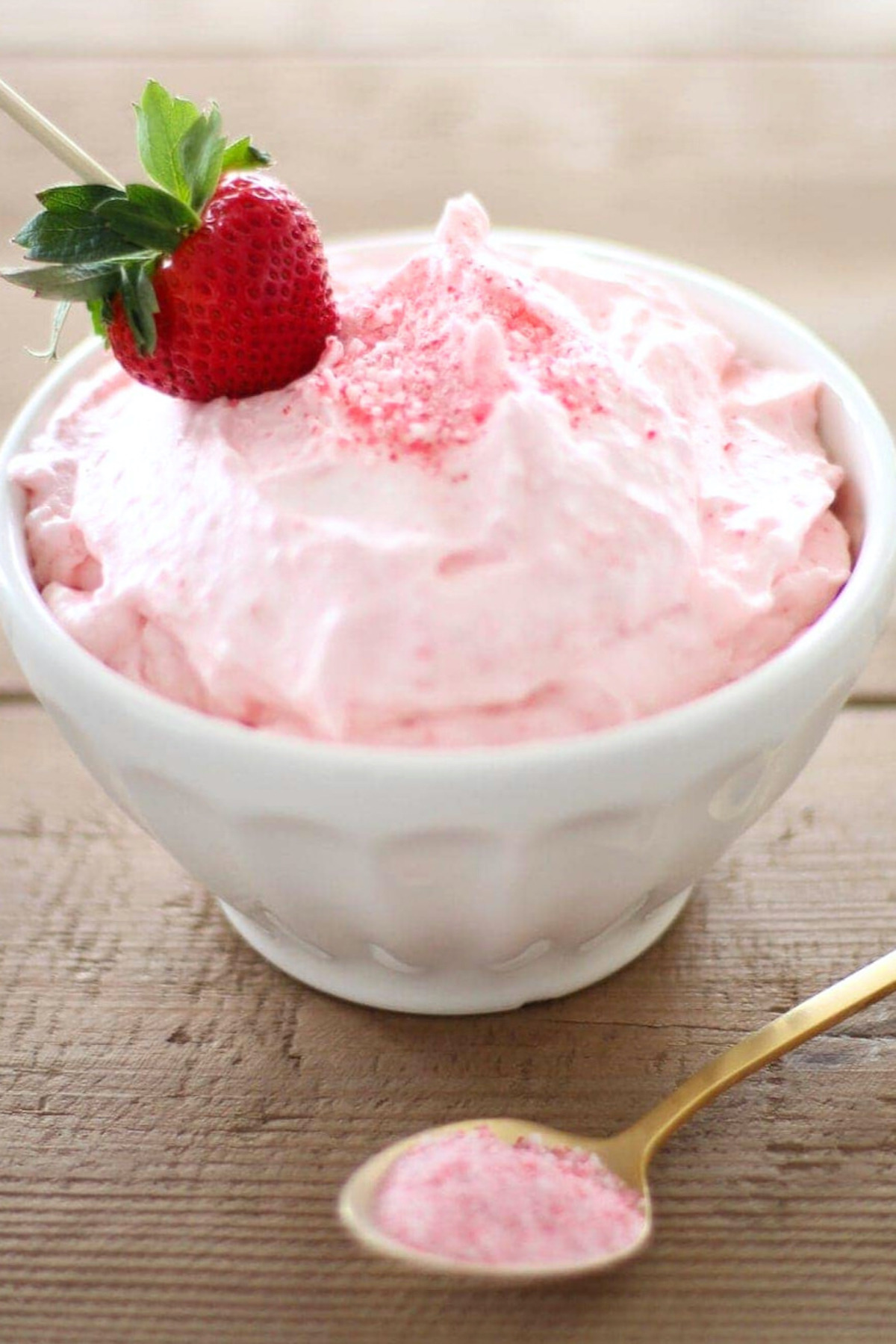 A bowl of strawberry whipped cream with a hint of peppermint flavor served with a gold spoon.