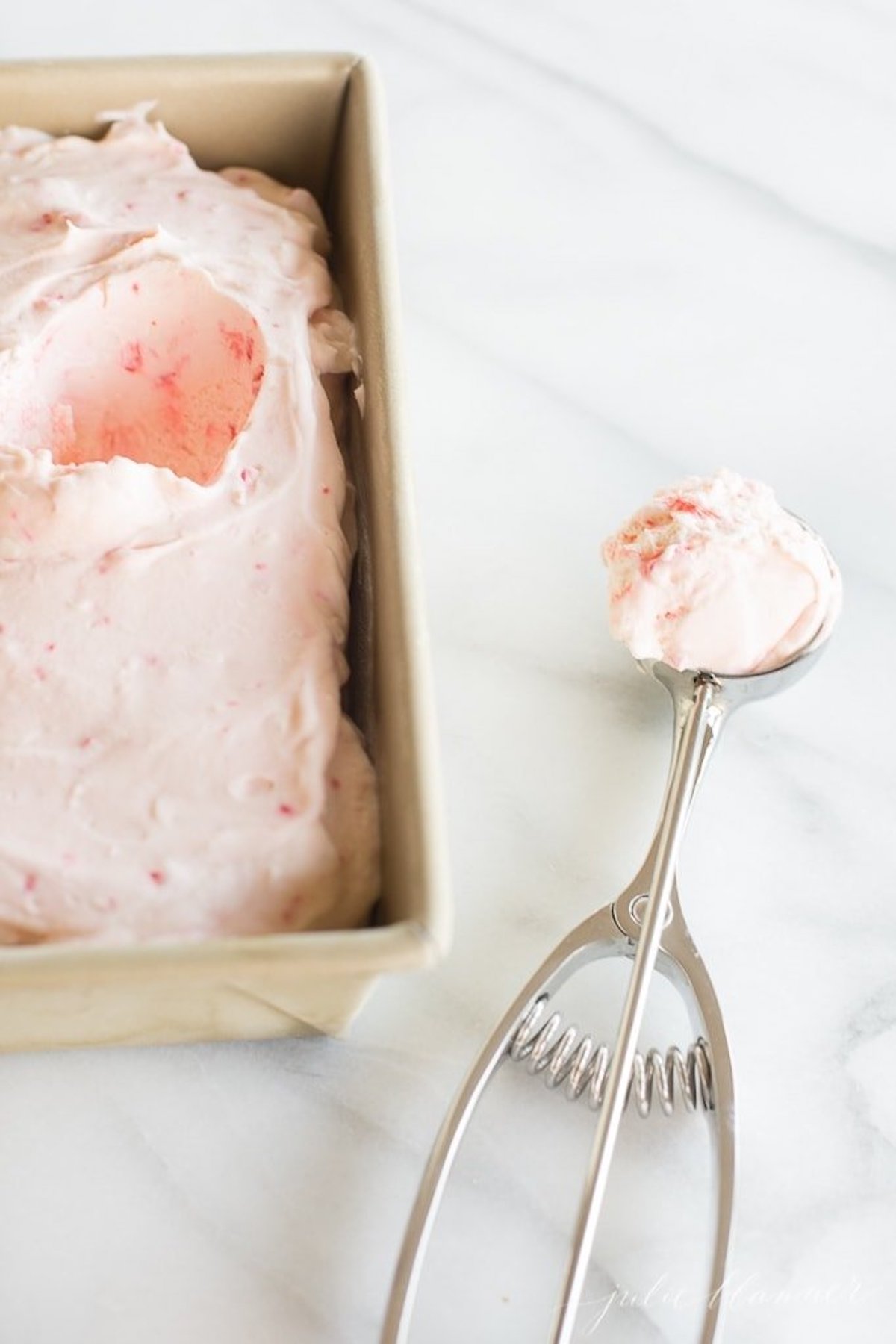 Peppermint-infused strawberry ice cream in a pan, expertly blended with a spatula.