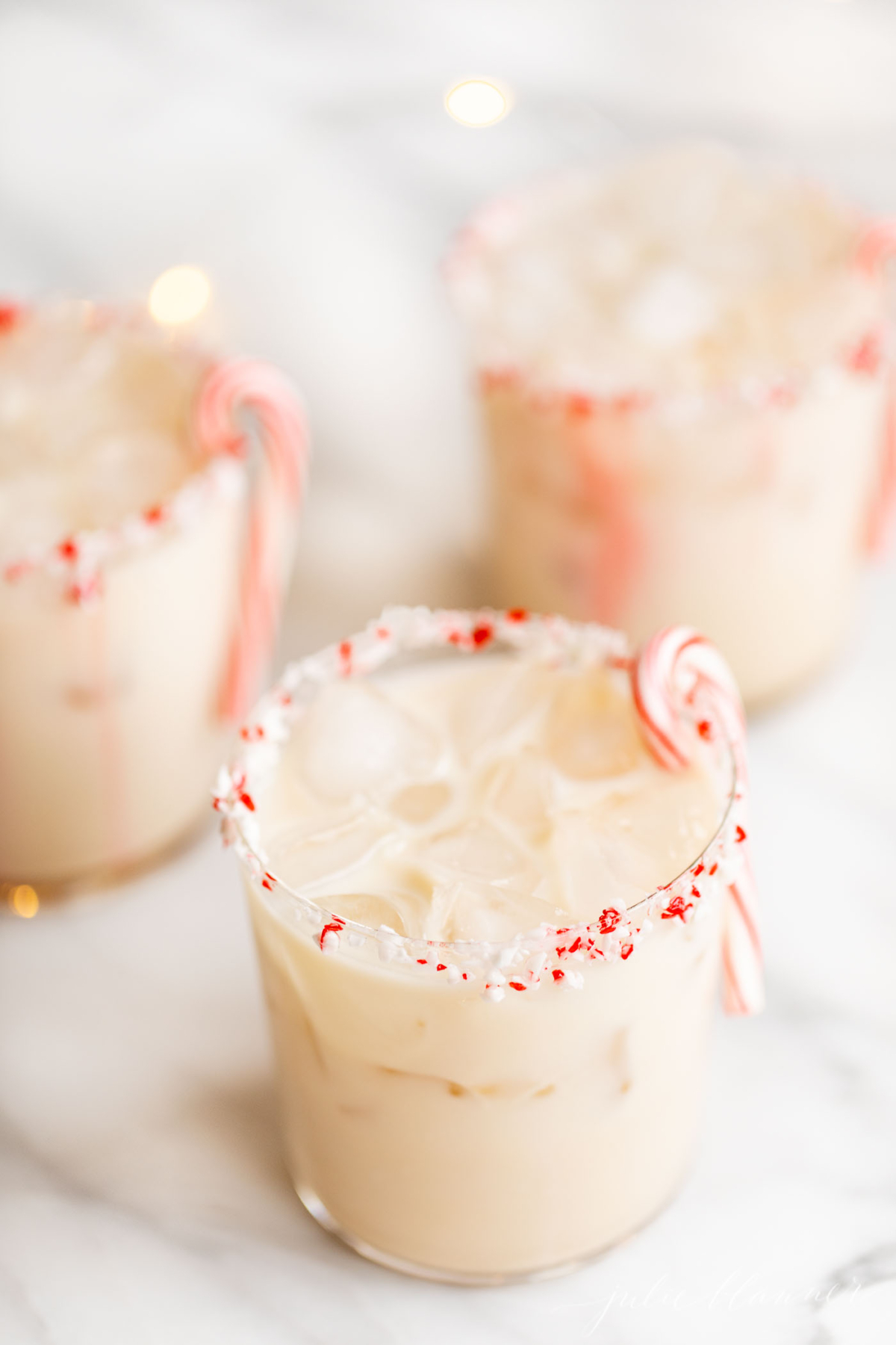 Three iced drinks with candy canes and peppermint extract on top.