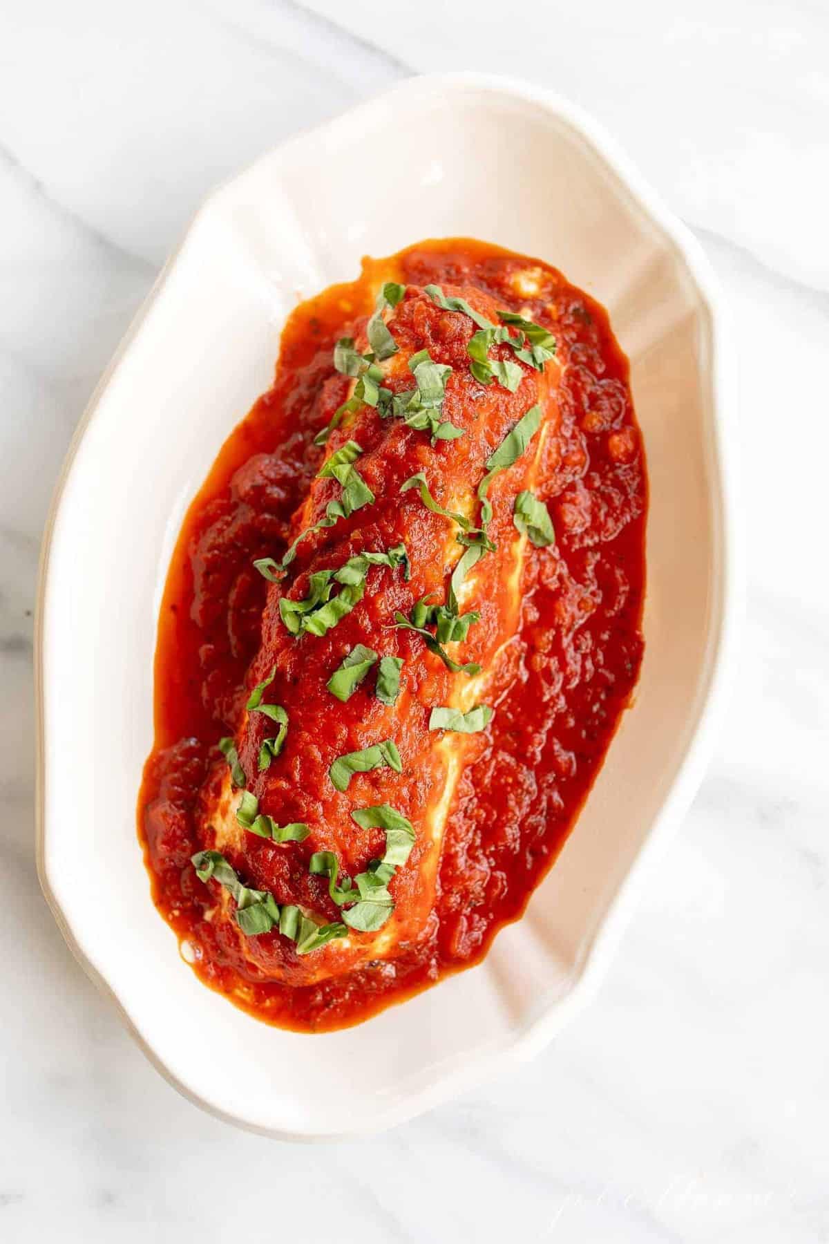 A single white serving dish filled with baked goat cheese covered in marinara.