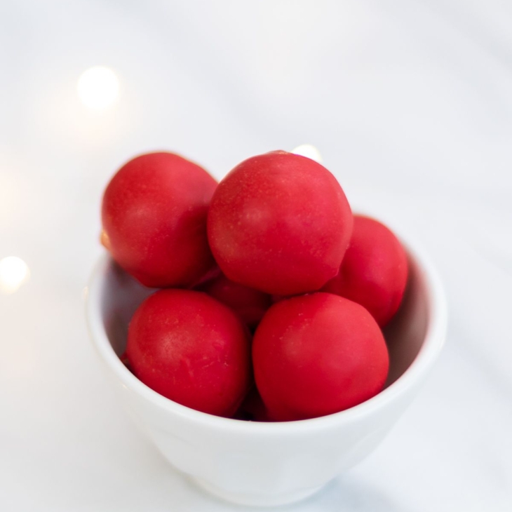 A white bowl full of red no bake Rudolph noses on a marble countertop.