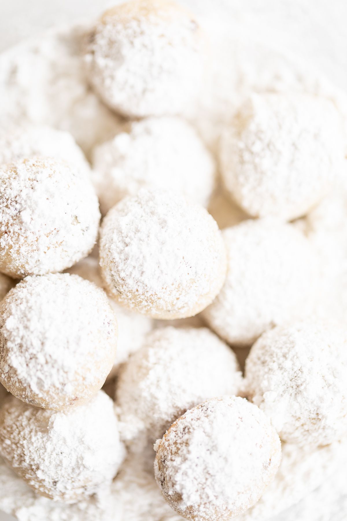 A white plate of chocolate chip pecan snowball cookies covered in powdered sugar.