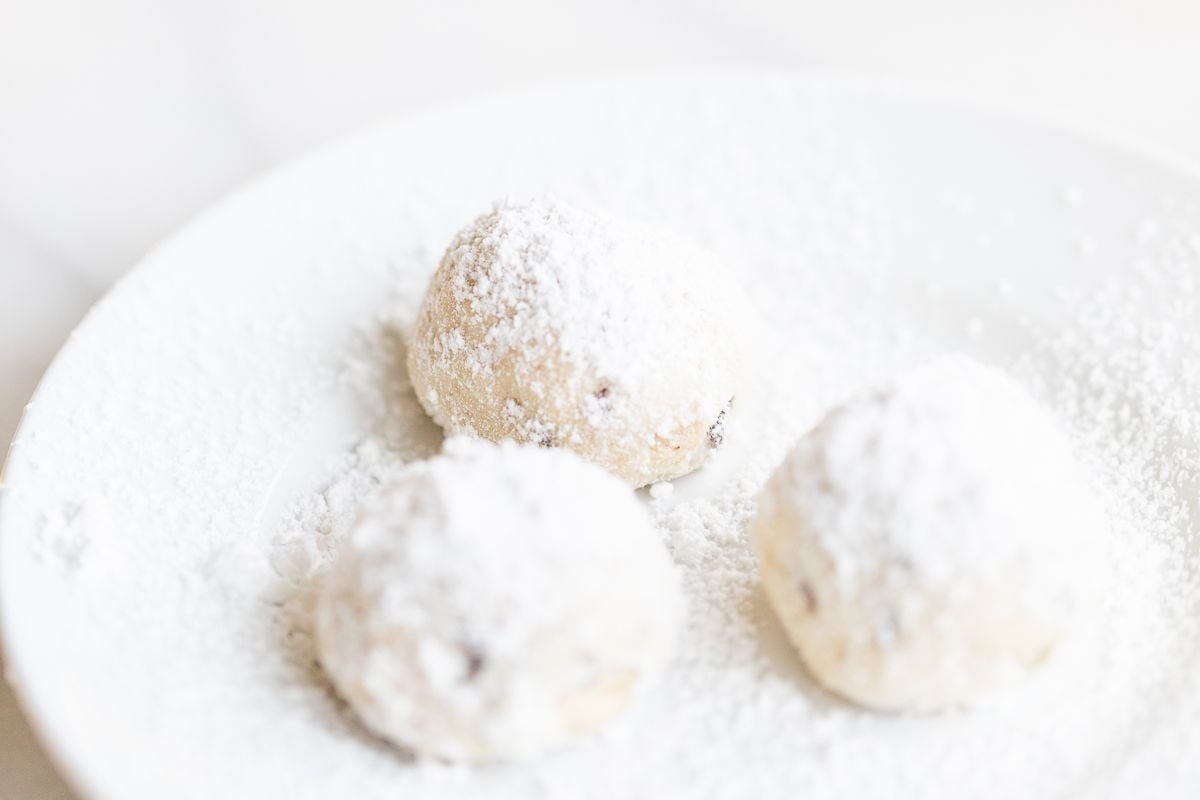 A white plate of pecan snowball cookies covered in powdered sugar.