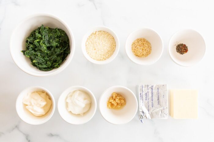 Ingredients for spinach dip with cream cheese laid out on a white surface.