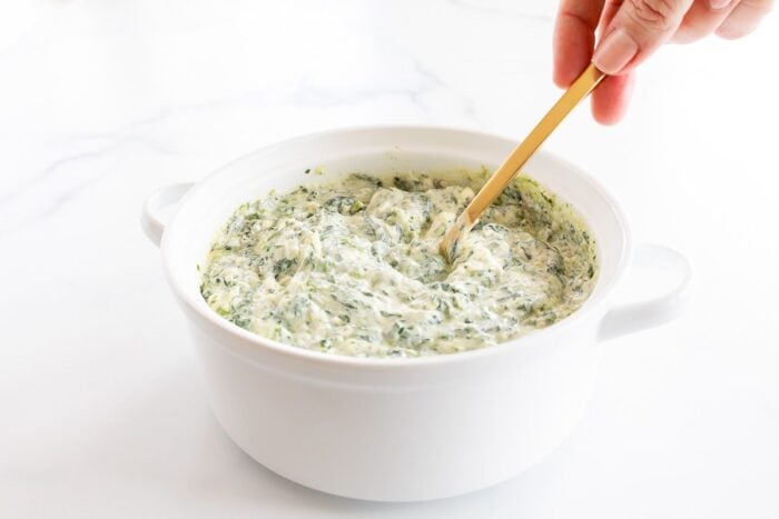 Cream cheese spinach dip being mixed in a white bowl.