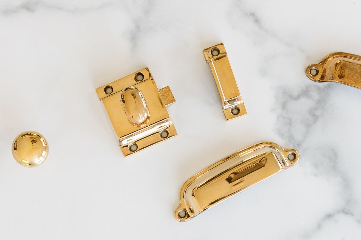Unlacquered brass hardware laid out on a marble countertop. 