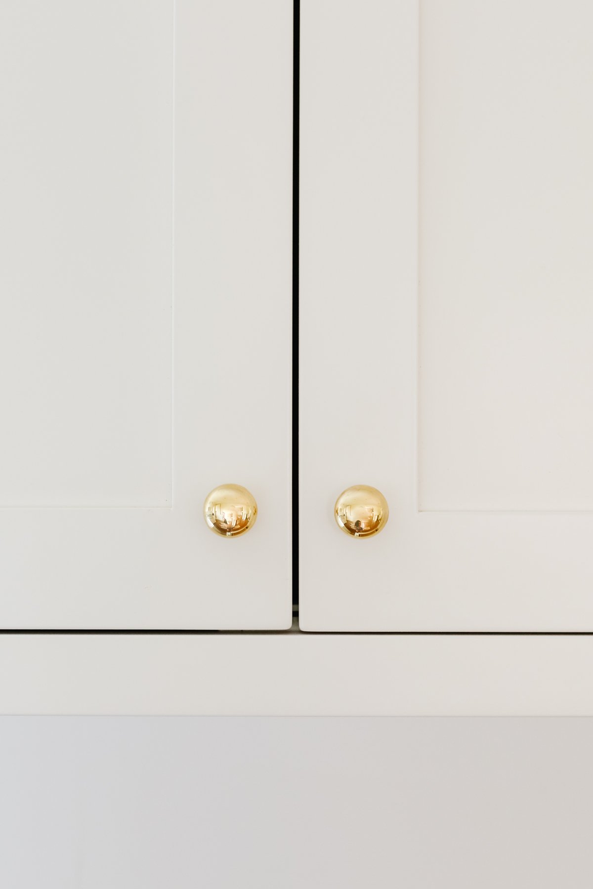 Cream kitchen cabinets with unlacquered brass hardware.