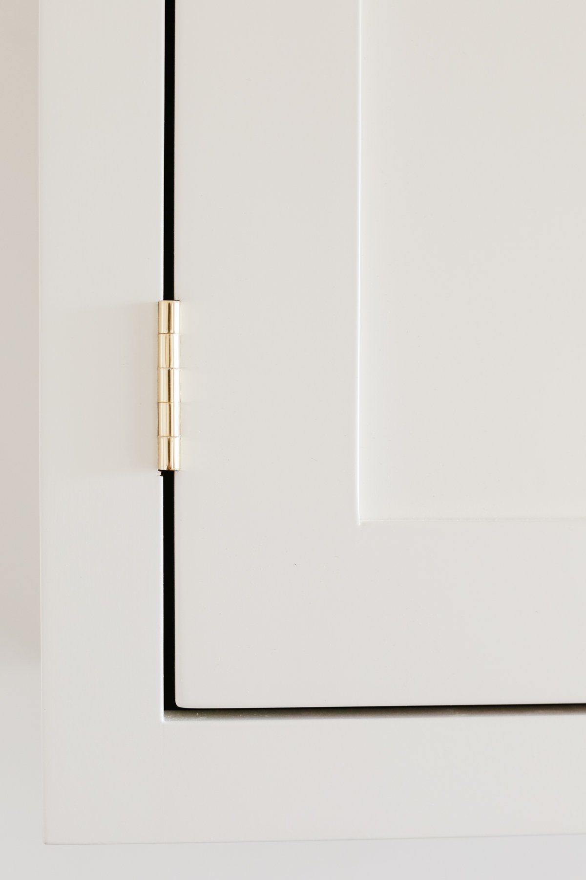 Cream kitchen cabinets with unlacquered brass hardware.