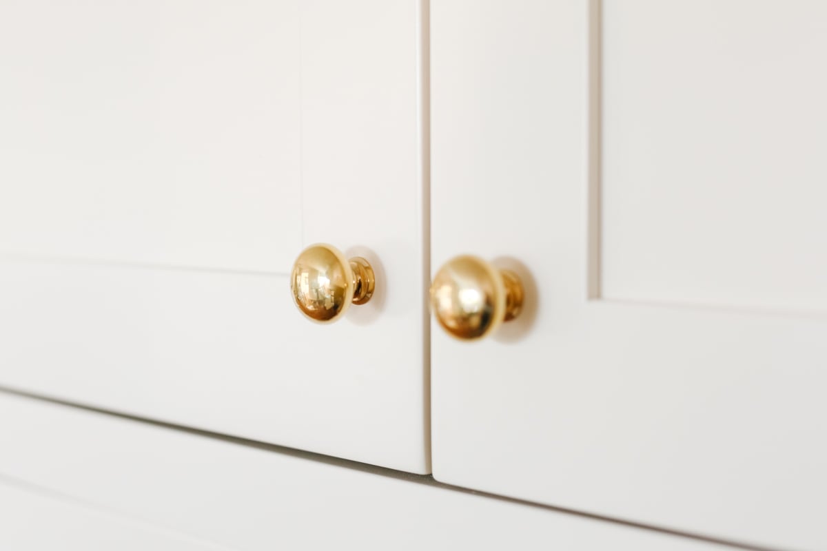 Cream kitchen cabinets with unlacquered brass hardware.