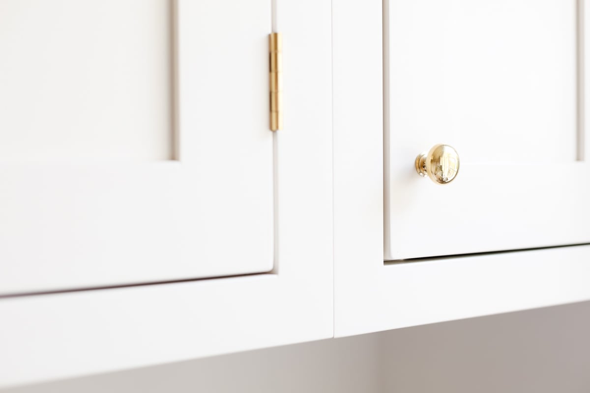 Cream kitchen cabinets with unlacquered brass hardware.