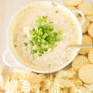 A bowl of bacon cheese dip with crackers and green onions.