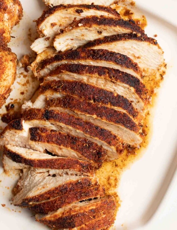 A white platter with sliced blackened chicken breasts.